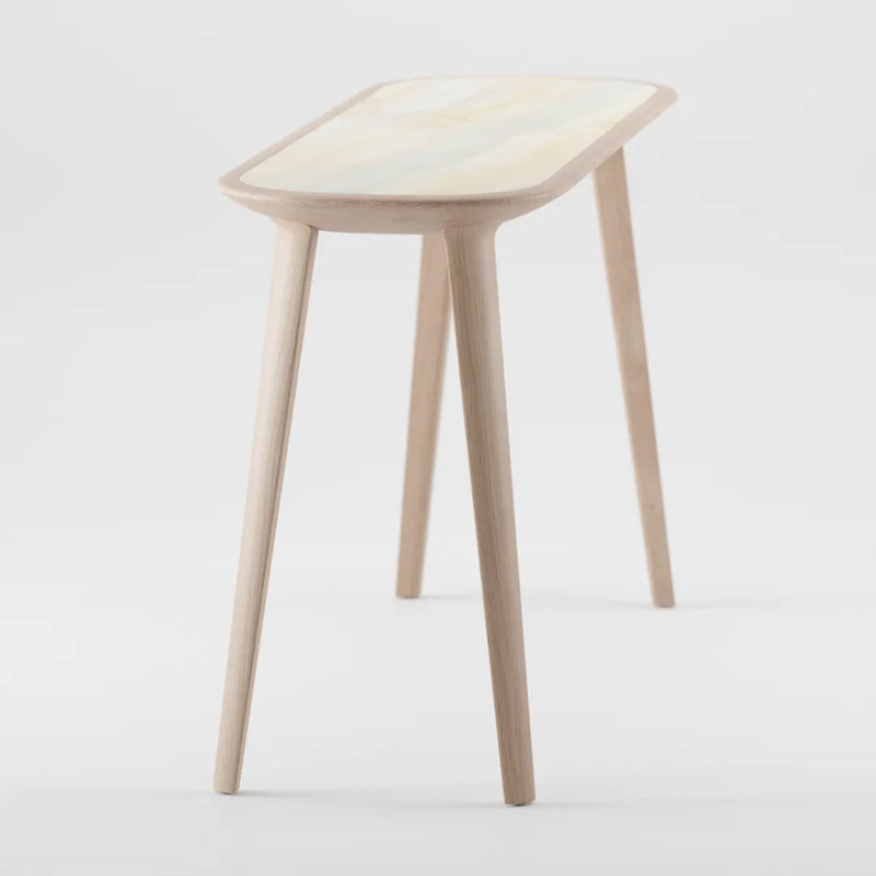 The KALOTA Console Table by Artisan showcases a minimalist design with three slender legs and a rectangular seat. Its light wood grain patterns stand out against a white background, highlighting the eco-friendly materials used.