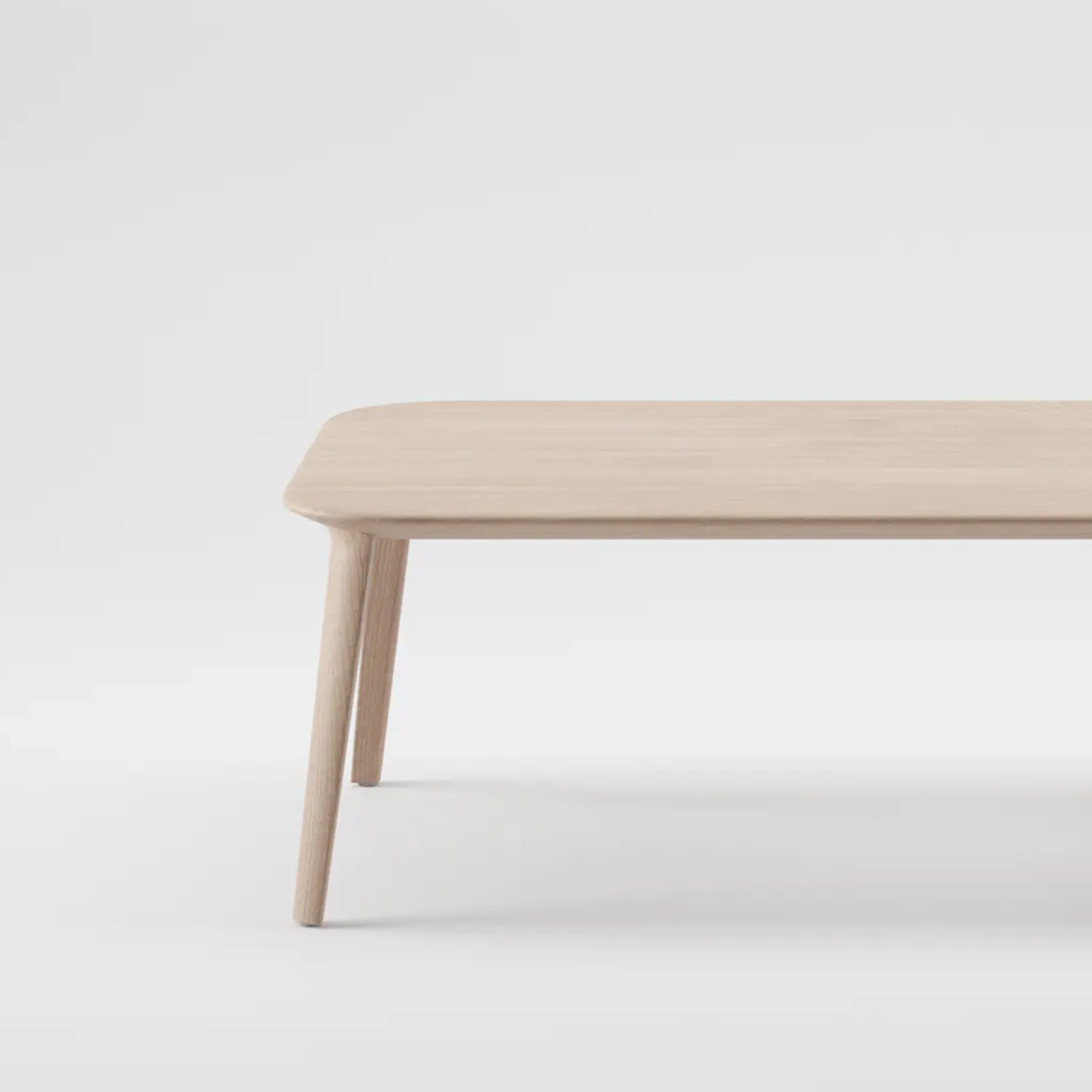 The KALOTA Coffee Table by Artisan is a minimalist piece crafted from solid wood, featuring a light natural finish. Its rectangular top has rounded edges and stands on four tapered legs, treated with natural oils to highlight its beauty, all constructed using environmentally-friendly materials.