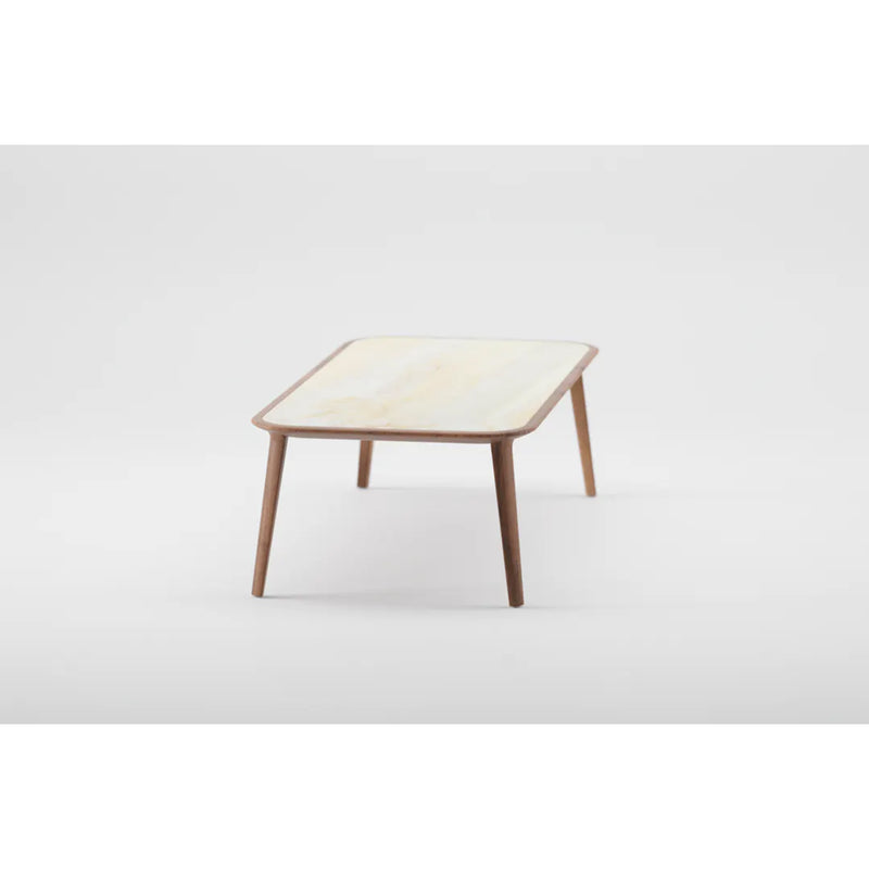 The KALOTA Coffee Table by Artisan is a minimalist piece crafted from solid wood, featuring a light-colored top and angled wooden legs finished with natural oils, set against a plain white background.