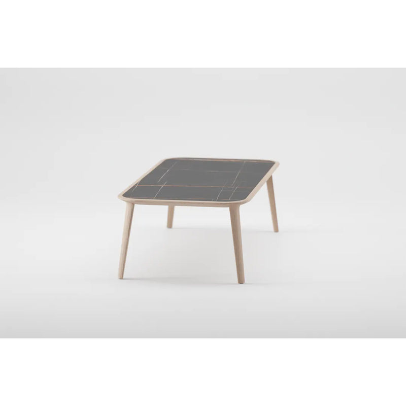 The KALOTA Coffee Table by Artisan features a minimalist design with slender legs and a dark, rectangular solid wood top adorned with a subtle grid pattern. Crafted from eco-friendly materials, it is showcased against a plain white background.