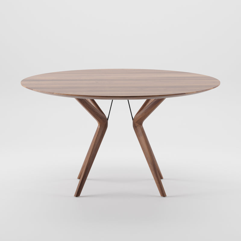 The Artisan LAKRI Round Table features a modern design with angled legs, crafted from solid wood with a smooth surface. Coated in natural oils, it stands against a white background, showcasing its contemporary style and eco-friendly materials.