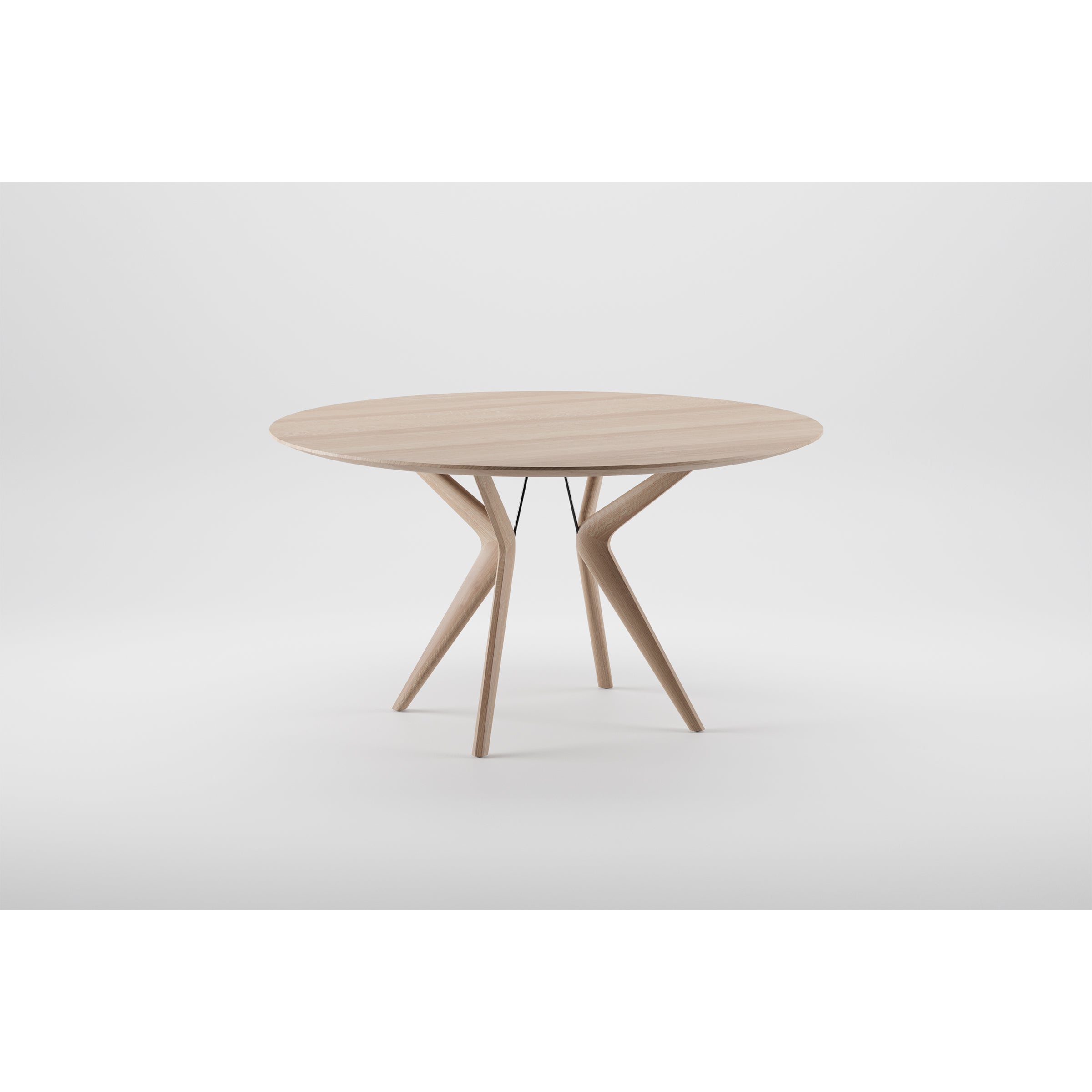 The LAKRI Round Table by Artisan is a modern wooden piece crafted from solid wood. It features a smooth top and a unique base with three angled legs that split into two branches, finished with natural oils, offering an artistic and elegant design against a plain white background.