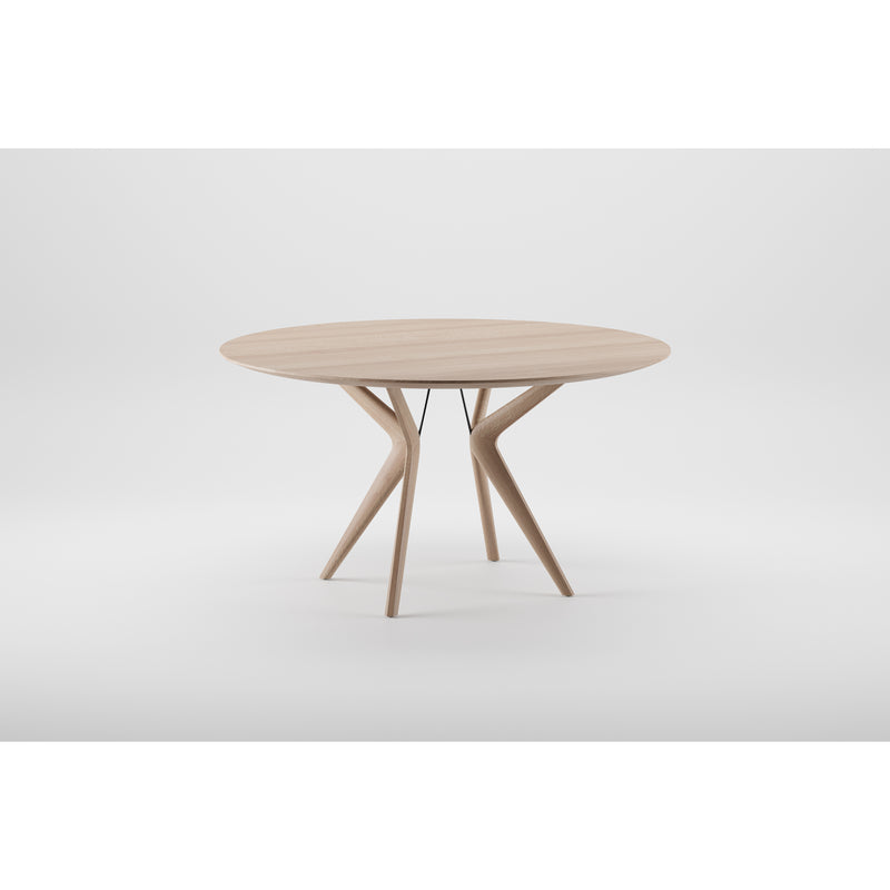 The LAKRI Round Table by Artisan is a modern wooden piece crafted from solid wood. It features a smooth top and a unique base with three angled legs that split into two branches, finished with natural oils, offering an artistic and elegant design against a plain white background.
