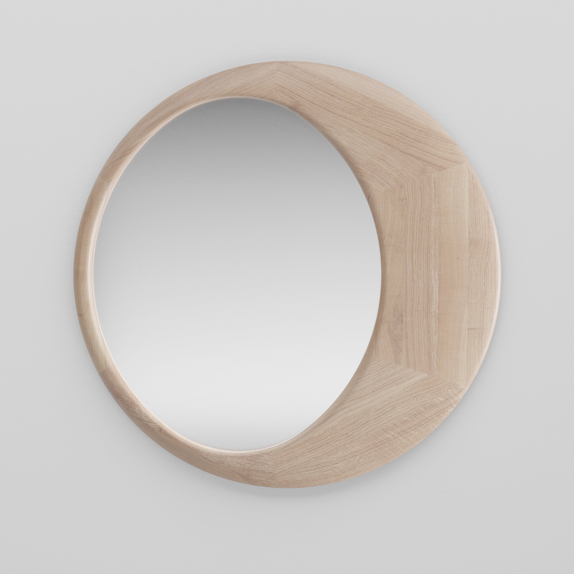 The Artisan Lana Mirror is circular, with a solid wood frame and unique design where the wood slightly overlaps the mirrors edge. Treated with natural oils, it offers a clear reflection against a white wall, made using eco-conscious materials.