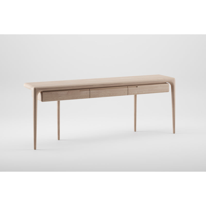 The Artisan LATUS Console table is a sleek, modern piece crafted from solid wood with minimalist design, featuring four slender legs and a smooth surface. It integrates three seamless front drawers, finished with natural oils, and is set against a plain white background.
