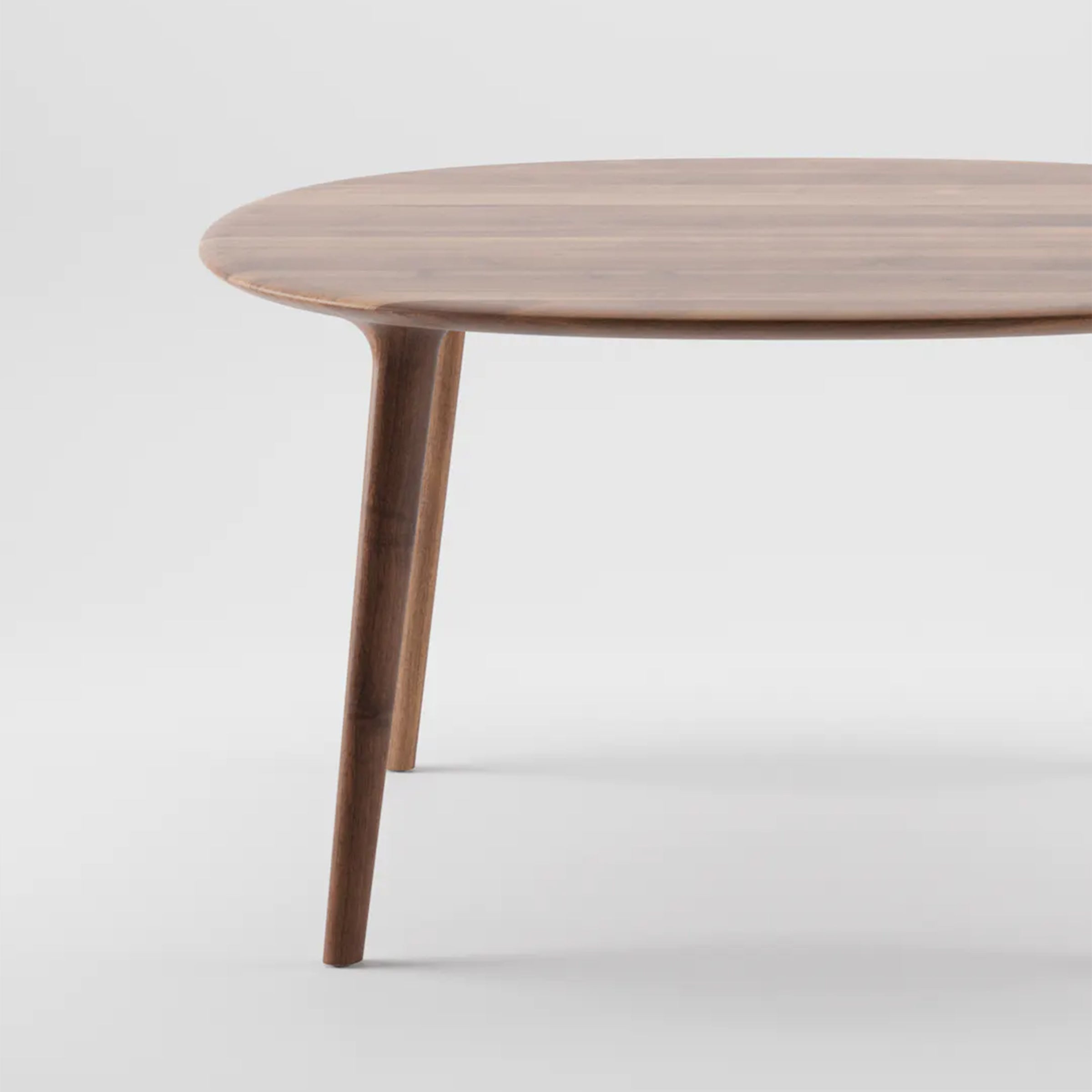 The LUC Table Round by Artisan embodies minimalist elegance with its smooth, round top and sleek, tapered legs. Crafted as artisanal wood furniture, it stands out against a light grey background highlighting its organic design.