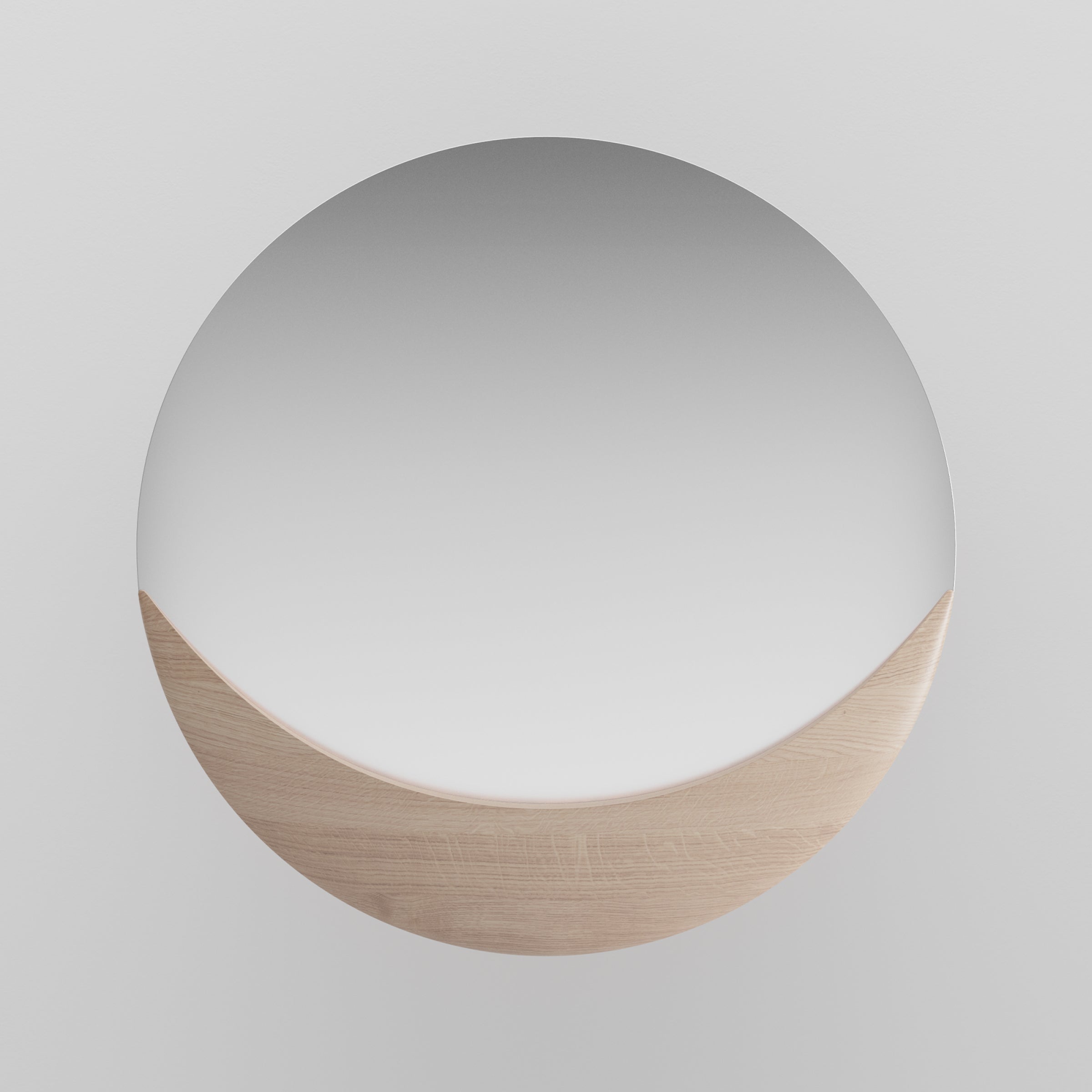 The Artisan Luna Mirror, featuring a minimalist round design mounted on a white wall, is enhanced by a solid wood semi-circle accent at the bottom. This detail artfully contrasts with the reflective surface, embodying the natural charm of wood.