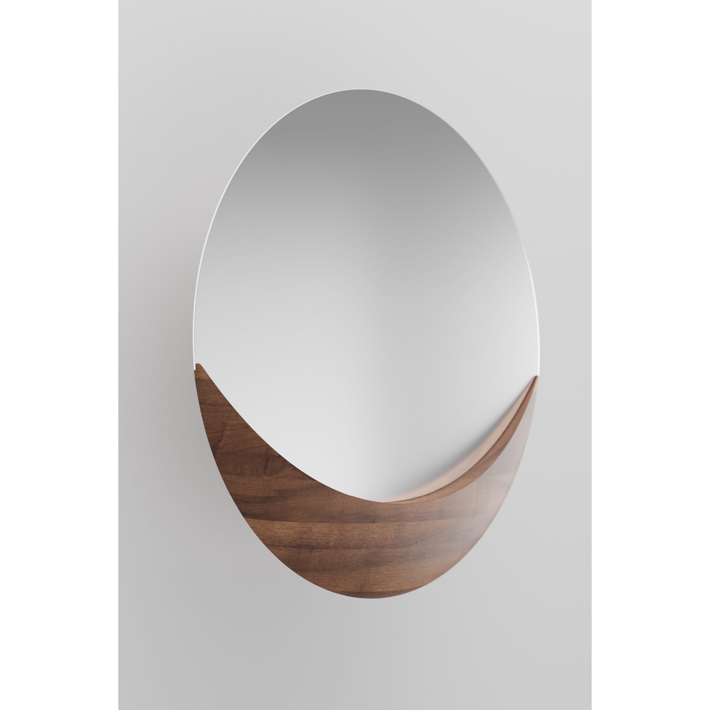 The Luna Mirror by Artisan, with its contemporary round shape and sleek solid wood accent at the bottom, is mounted on a plain white wall. It boasts a minimalist style and a smooth, polished surface crafted from environmentally-friendly materials.