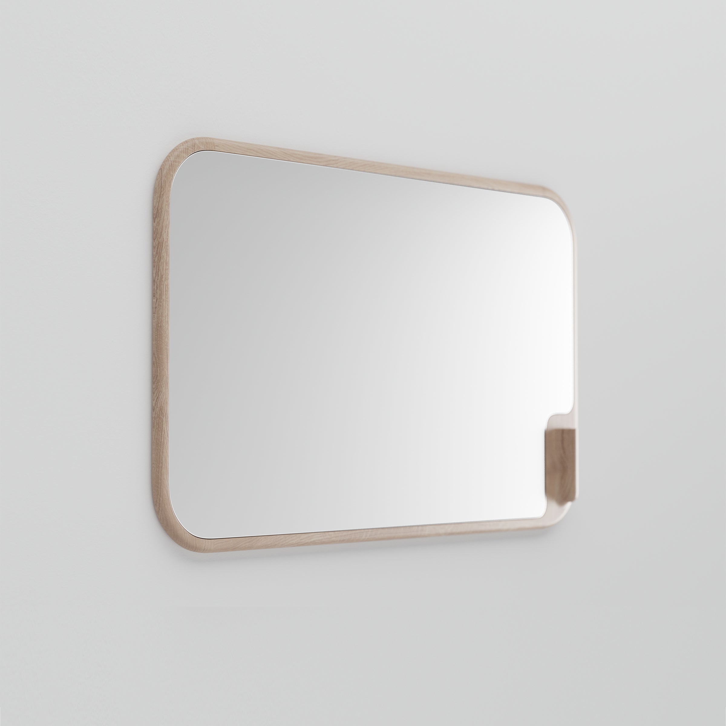The MUSE Mirror by Artisan is a rectangular mirror with rounded corners, mounted on a light grey wall. Made from solid wood and eco-friendly materials, its light wooden frame pairs beautifully with a small geometric wooden shelf on the right side.