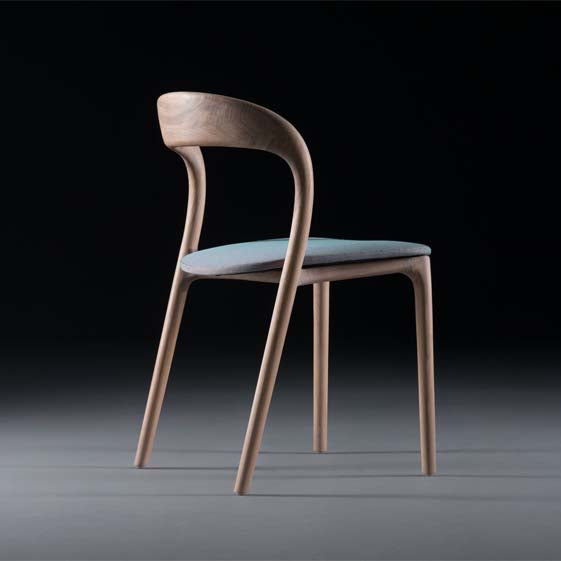 The NEVA light chair by Artisan is a sleek, modern wooden piece from the Neva collection, featuring a curved backrest and light blue cushioned seat, showcasing impeccable wood craftsmanship against a dark background.