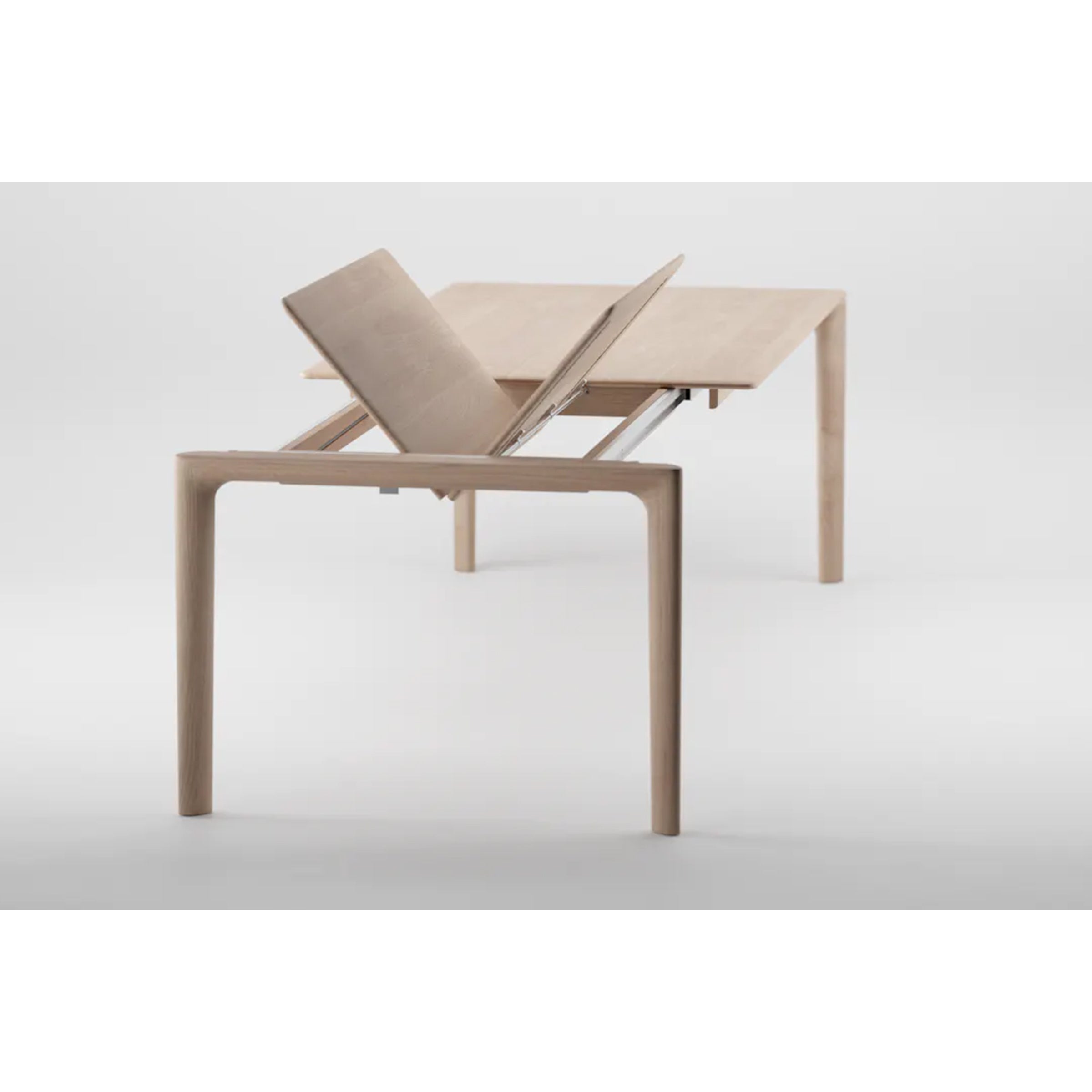 The Artisan NEVA Table Extendable, made from natural wood, features a light wood rectangular design with an artisanal handcrafted touch. A section lifts to reveal the extension mechanism, enhancing its expandable feature.