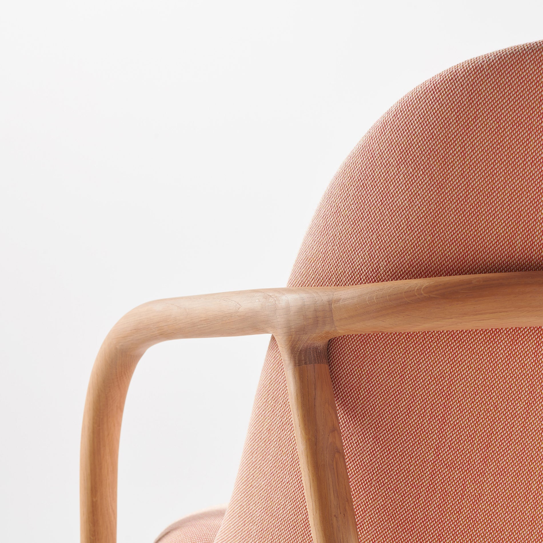 Close-up of the NEVA Lounge Chair Trimmed by Artisan, featuring a smooth, light wooden frame and soft pink upholstery. The focus is on the curved armrest and backrest, showcasing the artisanal craftsmanship and minimalist design against a plain white background.