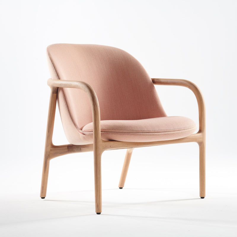 The NEVA Lounge Chair Trimmed by Artisan features a curved wooden frame and light pink upholstery on the seat and backrest, set against a plain white background.