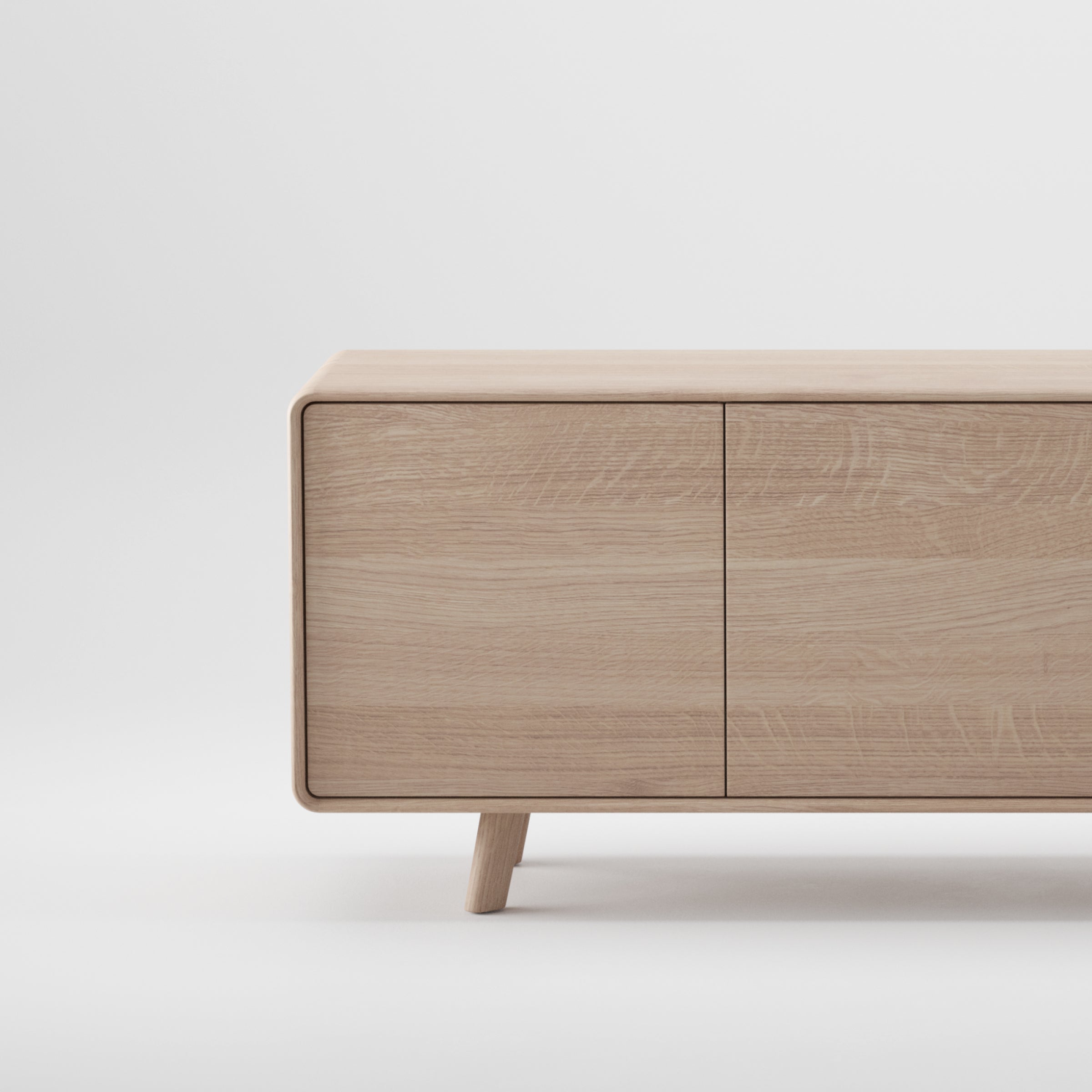 The NEVA Sideboard by Artisan is a minimalist cabinet with a light oak finish, featuring two doors and angled legs. The image showcases its simple, modern design and natural finishes against a plain white background.