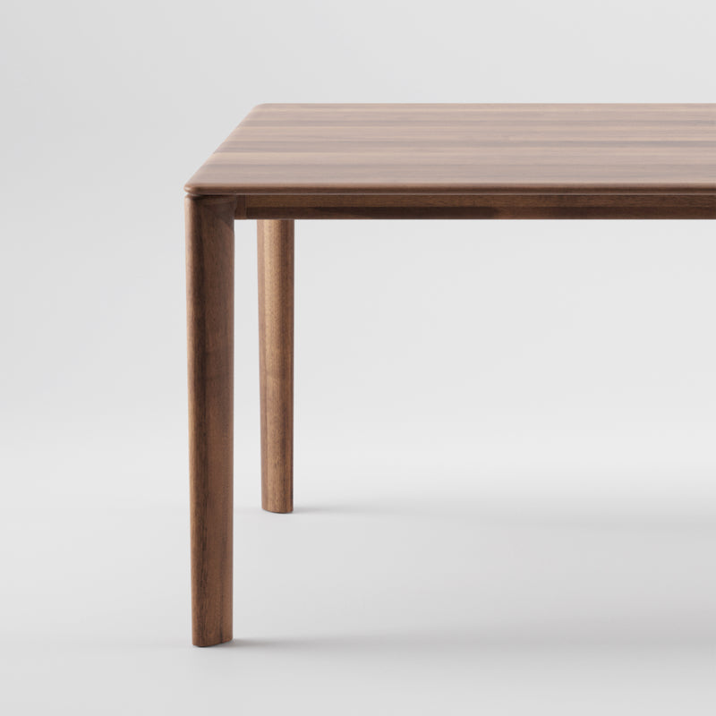 A close-up of the NEVA Table by Artisan highlights its smooth, straight legs. The tabletop features a natural wood grain finish and CNC carving, blending modern design with artisanal craftsmanship against a simple white backdrop.