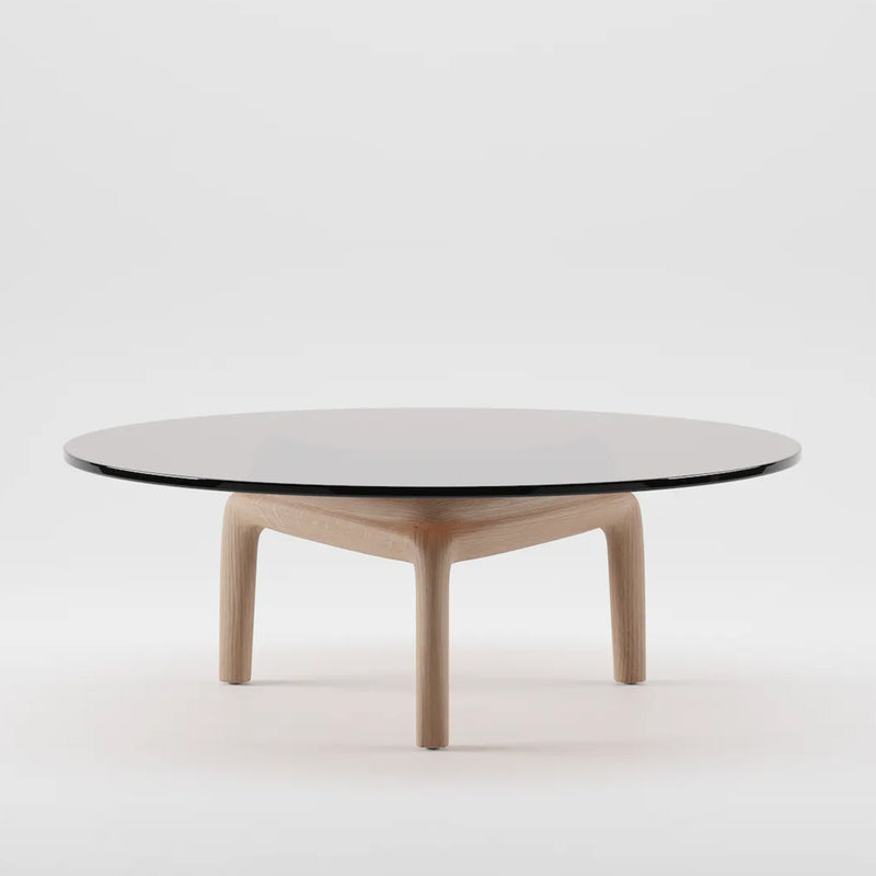 The PASCAL Coffee Table by Artisan features a minimalist design with a round black glass top and a light wooden base made from eco-friendly solid wood. Its three-legged structure creates a striking contrast against any white background.