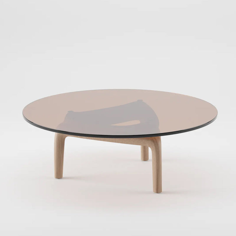 The PASCAL Coffee Table by Artisan features a round glass top with a solid wood base and three legs. Its minimalist design reflects light for a contemporary style against a white background, crafted from eco-friendly materials.