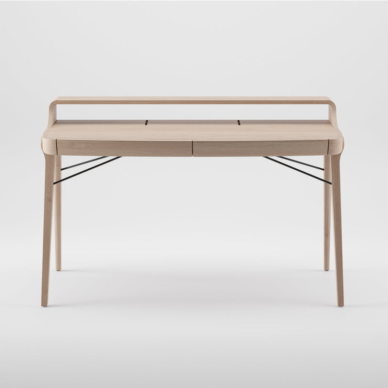 The Artisan PICARD Desk is a minimalist piece crafted from solid wood. It features four sleek legs, a raised back edge, subtle storage compartments, and black metal supports for added stability. Its plain light backdrop enhances its elegance and allows for customization.