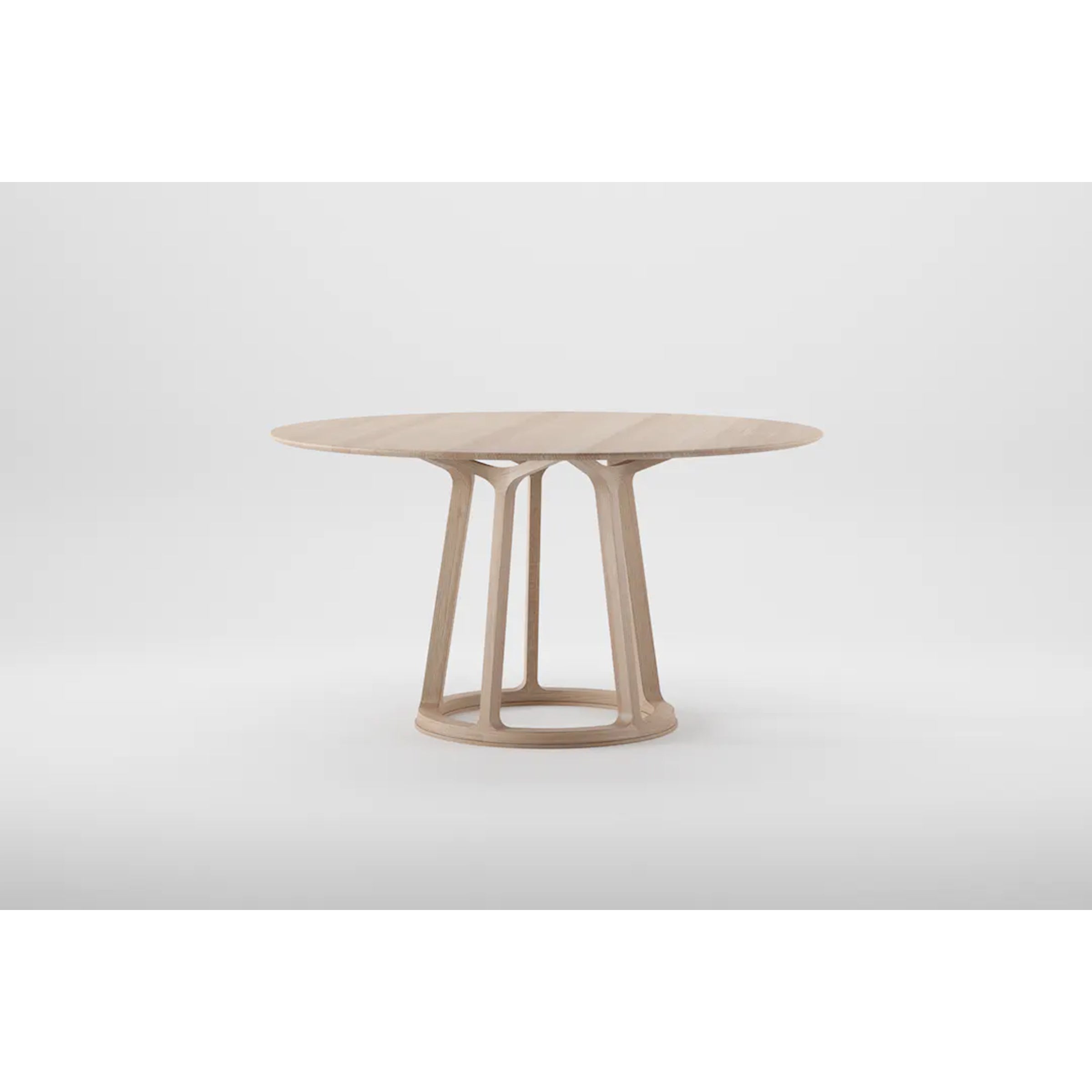 The PIVOT Round Table by Artisan is a round wooden table made from solid wood with a light finish. It has four angled supports on a circular base and is treated with natural oils for an eco-friendly design, standing out against the plain white background.