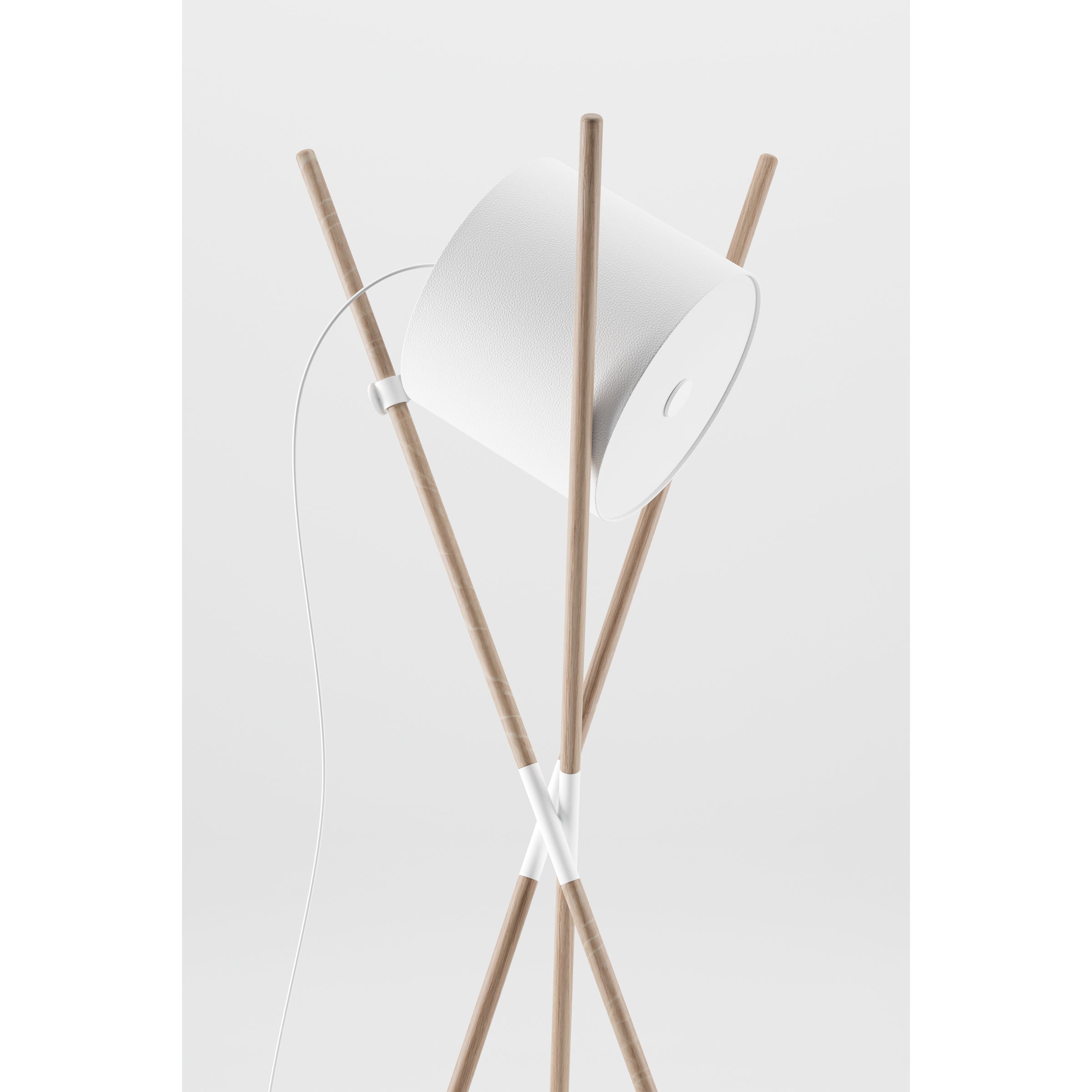The SHIFT Lamp by Artisan features a minimalist flat-pack design with a white cylindrical shade on four intersecting wooden struts, complemented by a trailing white cord against a light gray background.