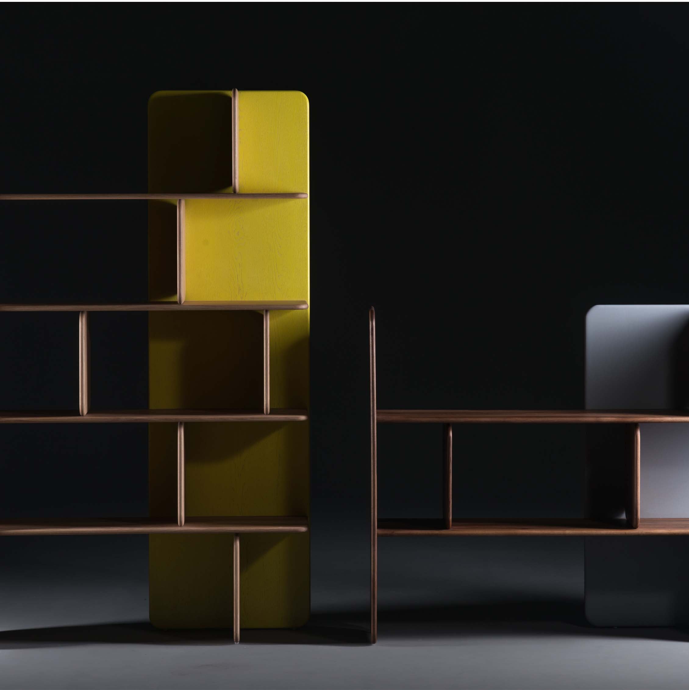 The Artisan SOFT Shelf - IVENTORY is a minimalist solid wood shelving unit with geometric shelves. It features a tall yellow back panel on one side and a shorter gray one on the other, offering an abstract modern design with natural finishes against a dark background.