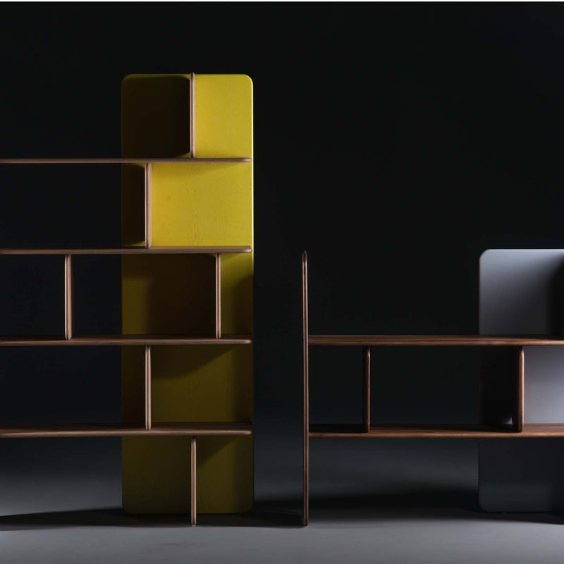 The Artisan SOFT Shelf - IVENTORY is a minimalist solid wood shelving unit with geometric shelves. It features a tall yellow back panel on one side and a shorter gray one on the other, offering an abstract modern design with natural finishes against a dark background.