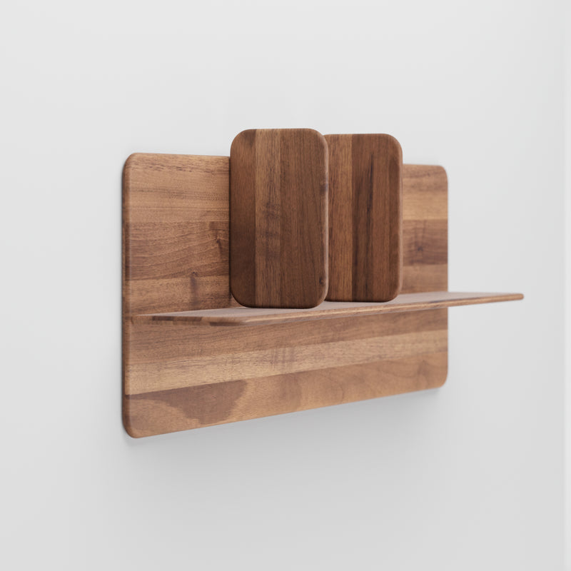 An Artisan Soft Wall Module is elegantly mounted on a white wall, featuring a minimalist design with a rectangular base and two upright supports made of organic wood in a light brown finish that highlights the grain patterns.