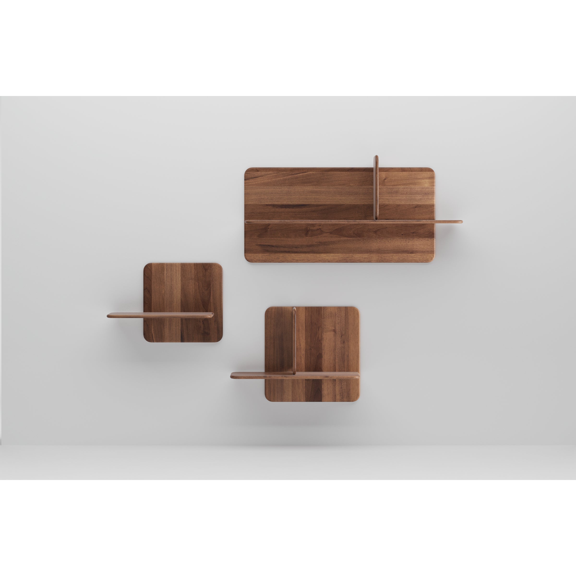 Part of Artisans Soft Wall Modules collection, these three wall-mounted shelves feature a minimalist design on a white wall. Made from organic wood, the set includes one large rectangular shelf and two smaller square ones, each with a vertical divider.