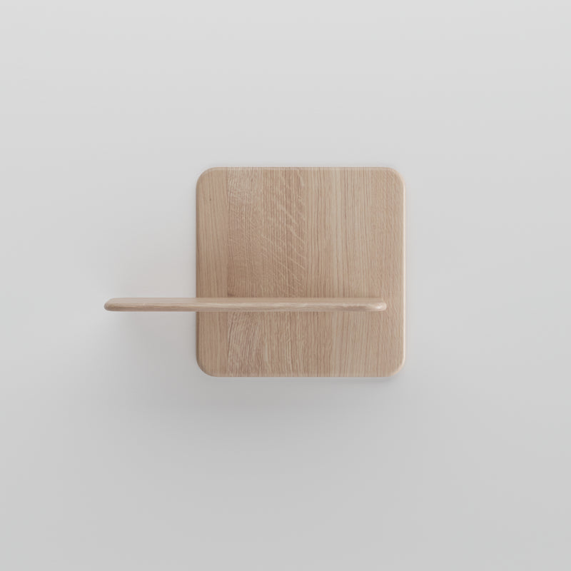 The Soft Wall Modules by Artisan showcase a minimalist wooden shelf with a rectangular base and horizontal ledge, perfect for mounting on a white wall. Crafted from organic materials, it has a light natural finish, highlighting the woods elegance in its simplest form.