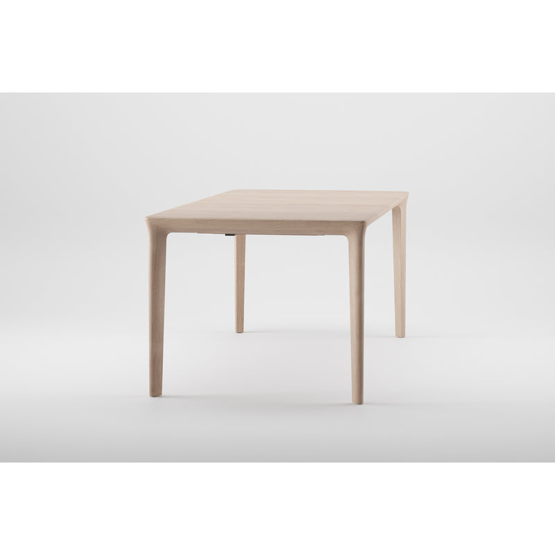 The TARA Extendable Table by Artisan showcases a sleek design with a minimalist, light-finished solid wood top and slender tapered legs, all set against a plain white background. Its organic beauty lends a modern and stylish touch to any space.