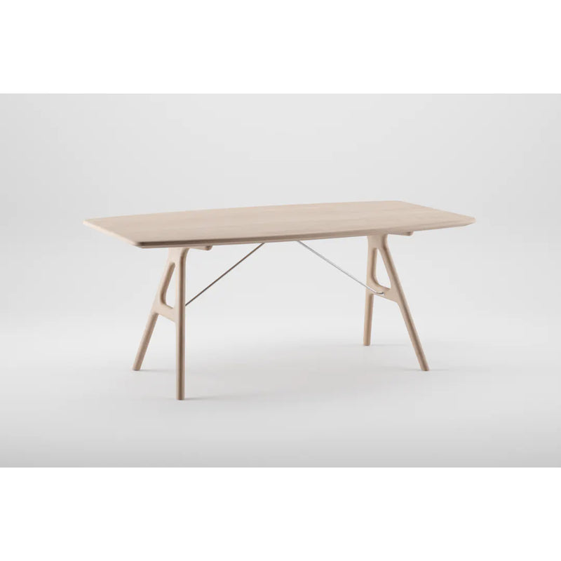 The TESA Table by Artisan is a modern rectangular piece crafted from eco-friendly solid wood, featuring a light finish, sleek angled legs, and a subtle metal support bar. It stands elegantly on a plain white background.