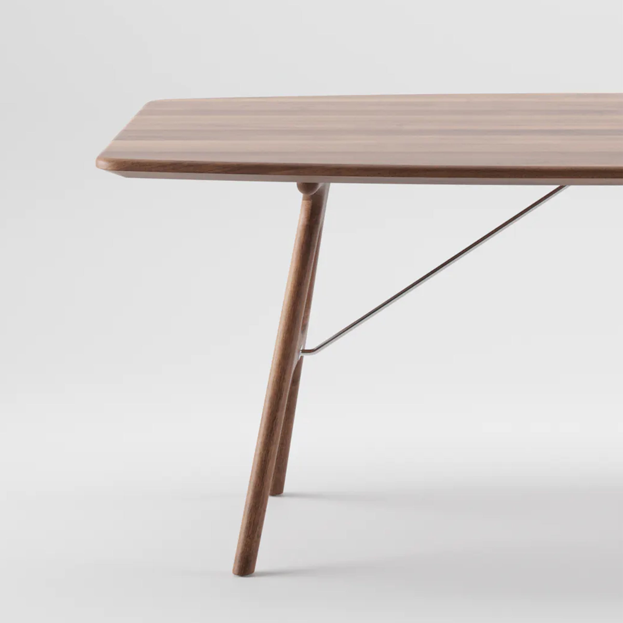 The image features the TESA Table by Artisan, a minimalist piece crafted from solid wood. It has a smooth, rectangular top and angled legs supported by a metal brace. Finished with natural oils, the table complements the simple light gray background.