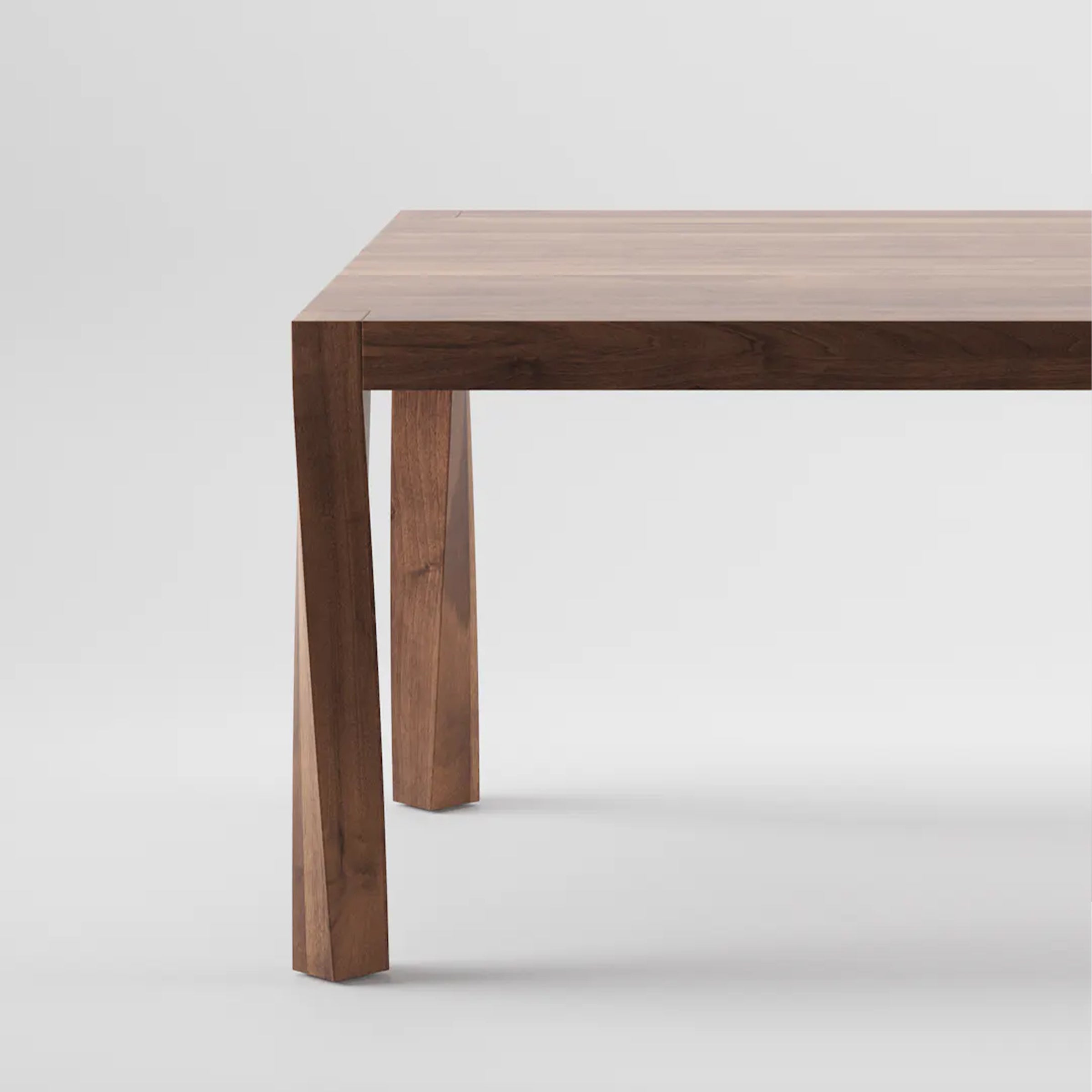 A close-up of the Artisan TOR Table corner highlights its smooth, polished surface and sturdy solid wood legs. The natural brown finish accentuates its grain and organic beauty, while a plain white background emphasizes its minimalist design.