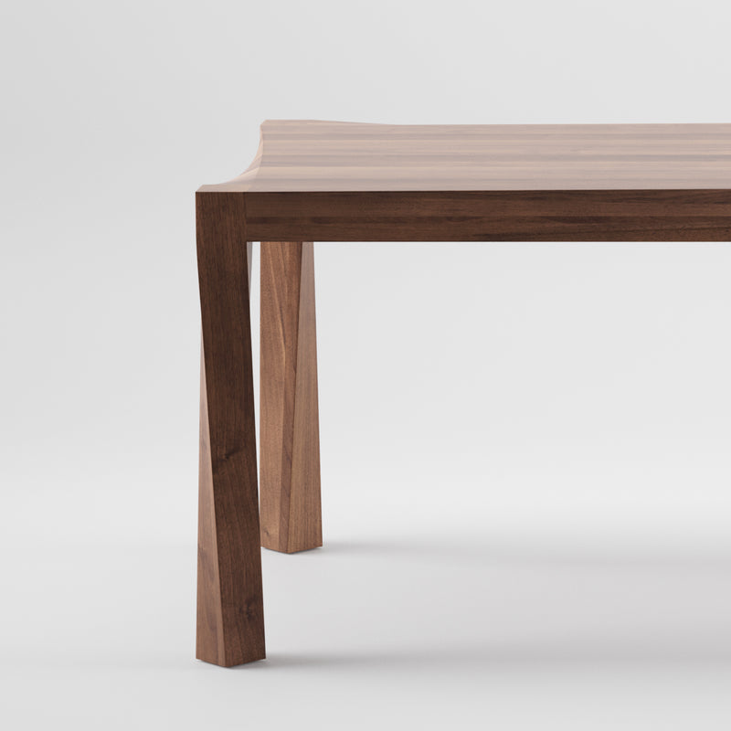 A close-up of the TORSIO Table by Artisan showcases its modern craftsmanship from solid wood, featuring a smooth surface and clean lines. The slightly angled legs introduce subtle design, while natural oils enhance the rich finish against a neutral backdrop.