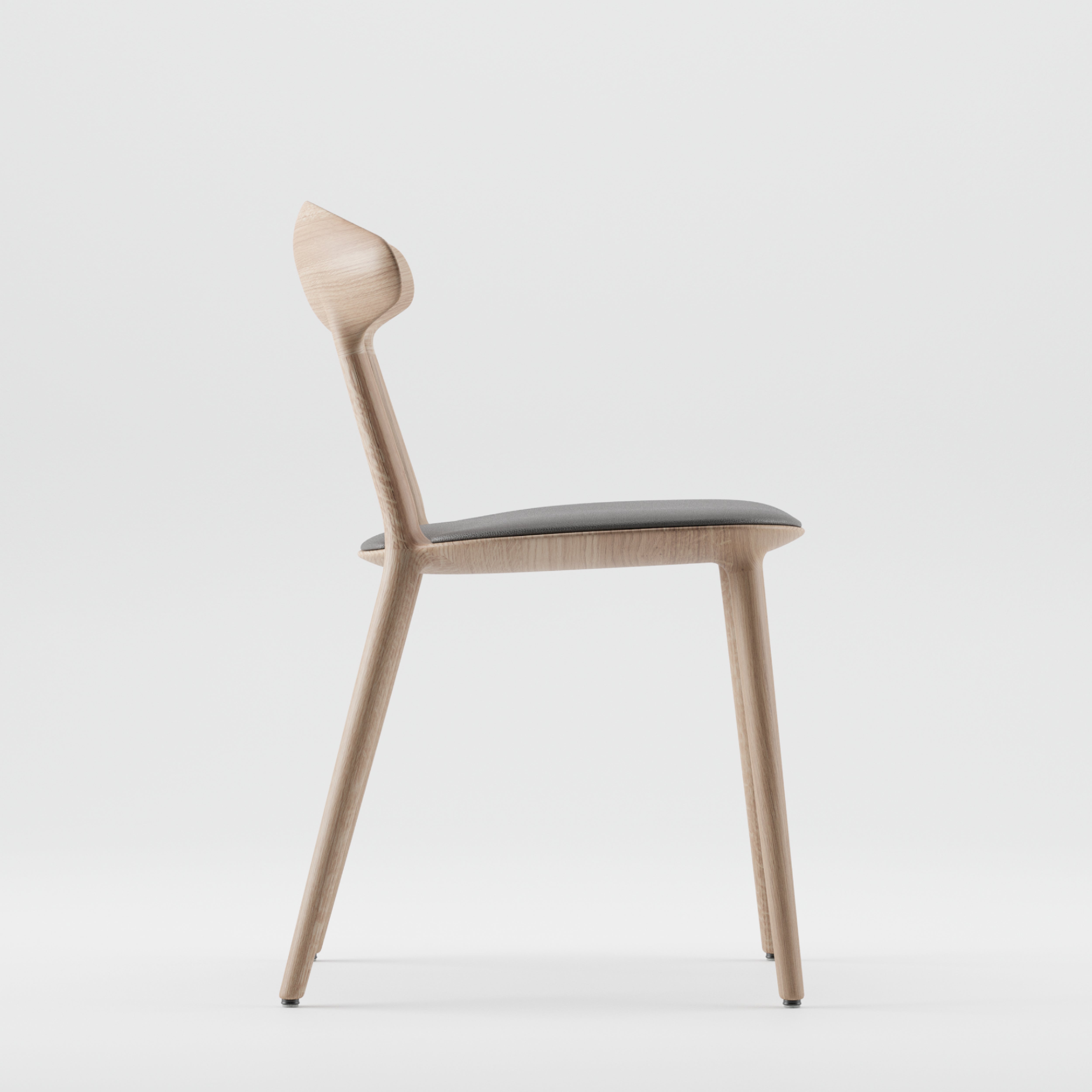 The Artisan WU Chair Upholstered is a minimalist piece crafted from solid wood. It features a curved backrest, angled legs enhanced with natural oils, and a sleek black cushioned seat, all set against a plain white background.