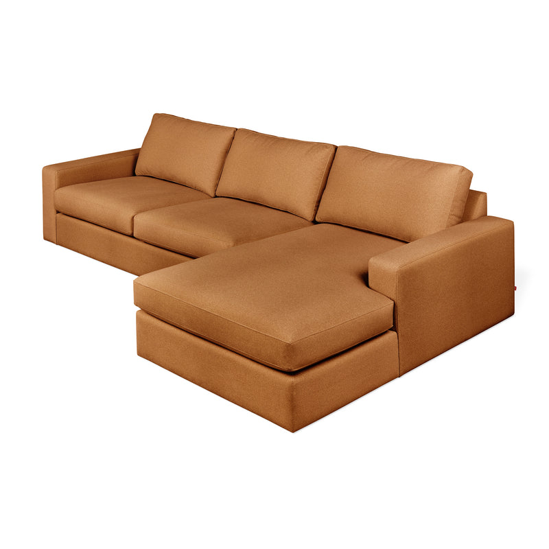 The Ashdale Right-Facing Sectional by Gus Modern features a sturdy hardwood frame, three synthetic-down back cushions, wide armrests, and solid tan upholstery. Its chaise lounge extends to the right for modern minimalist comfort.