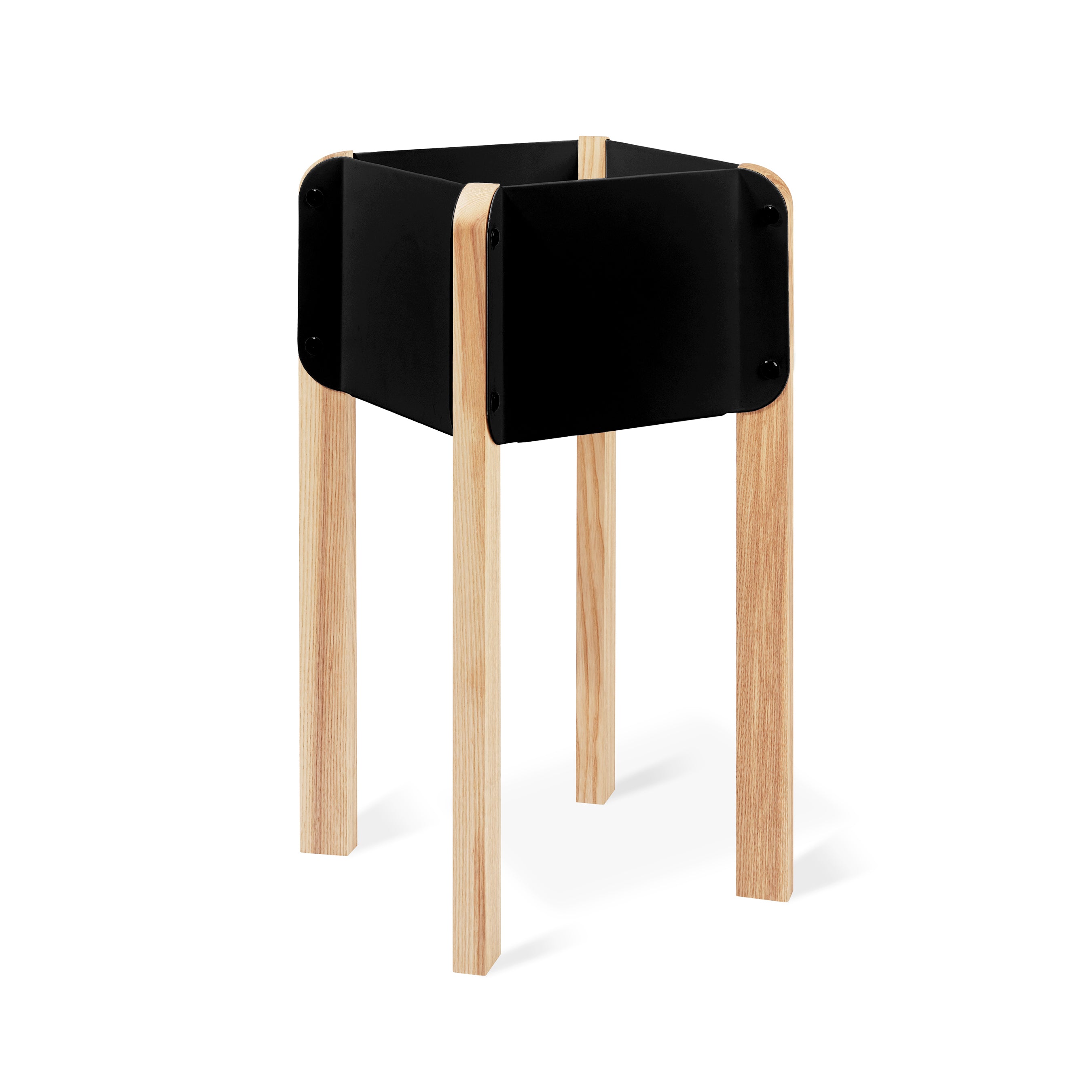 The Atrium Planter Hi by Gus Modern features Bauhaus-inspired design, with four light wood legs supporting a square black planter box elevated stylishly above the ground.