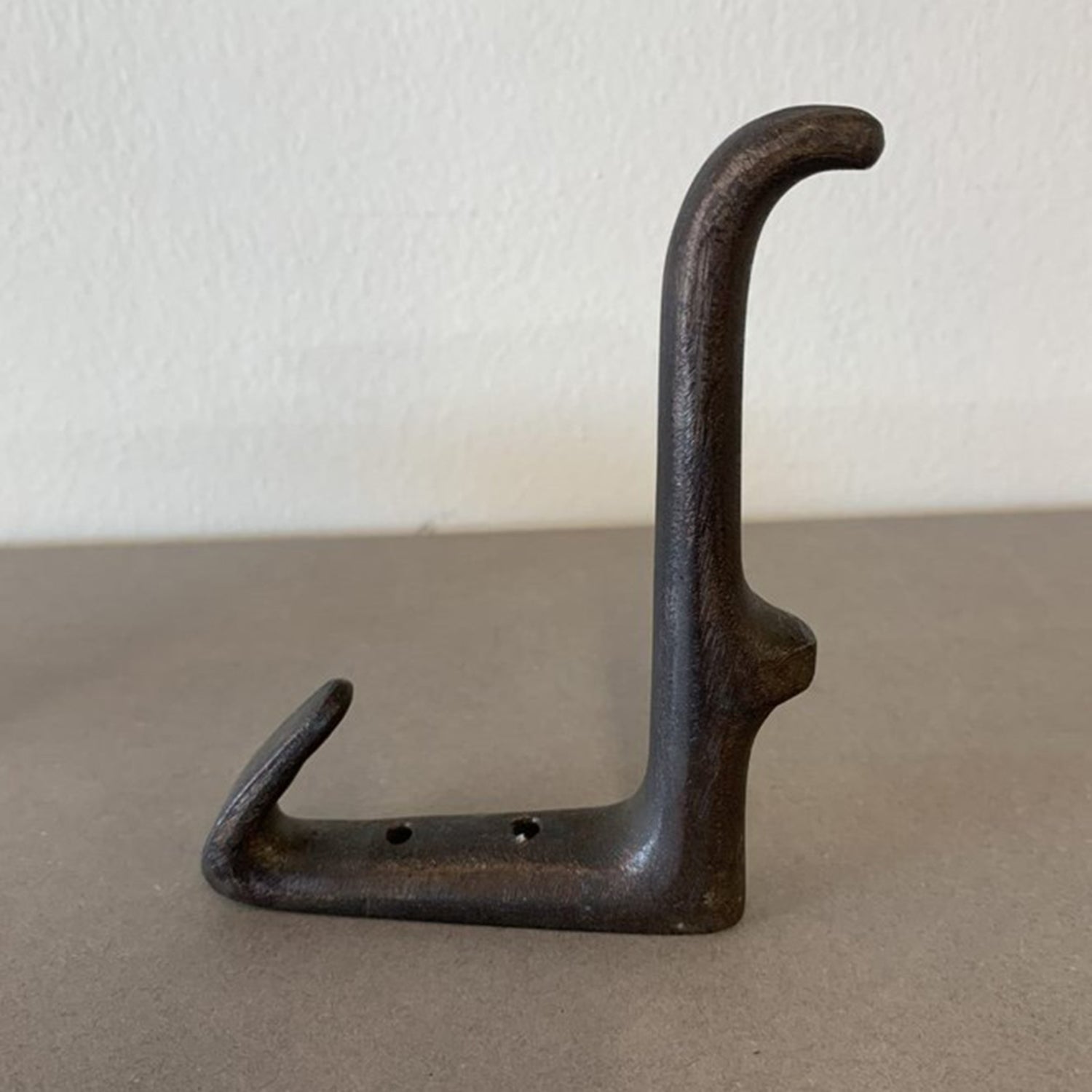 Hook #4965 - Sale by Werkstätte Carl Auböck is a vintage cast iron wall hook with a textured surface, featuring two curves and screw holes for mounting. Its weathered metal and classic design evoke the charm of a Viennese townhouse.
