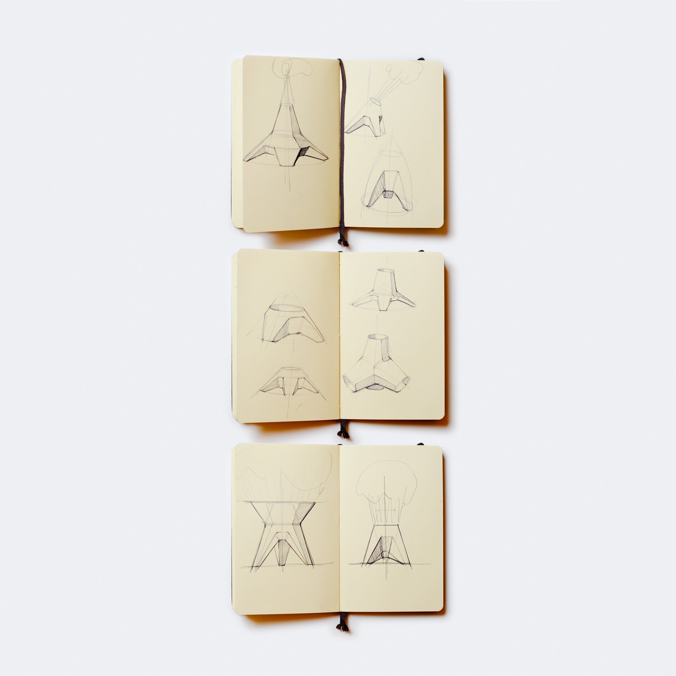 Three open sketchbooks reveal pencil drawings of geometric and architectural designs on a light background, showcasing various angles and perspectives reminiscent of the innovative style found in Augartens Rocket Vase.