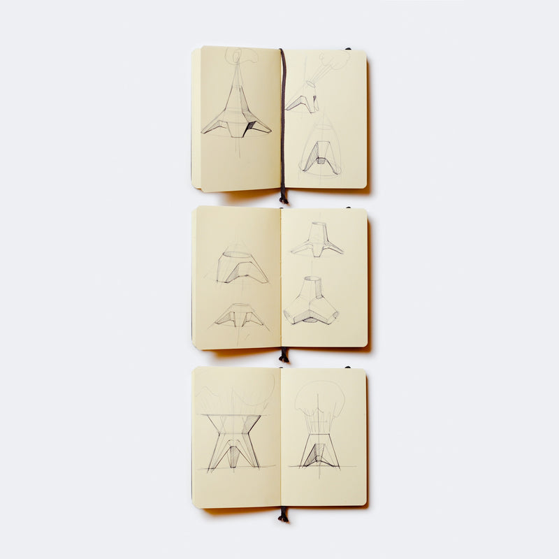 Three open sketchbooks reveal pencil drawings of geometric and architectural designs on a light background, showcasing various angles and perspectives reminiscent of the innovative style found in Augartens Rocket Vase.