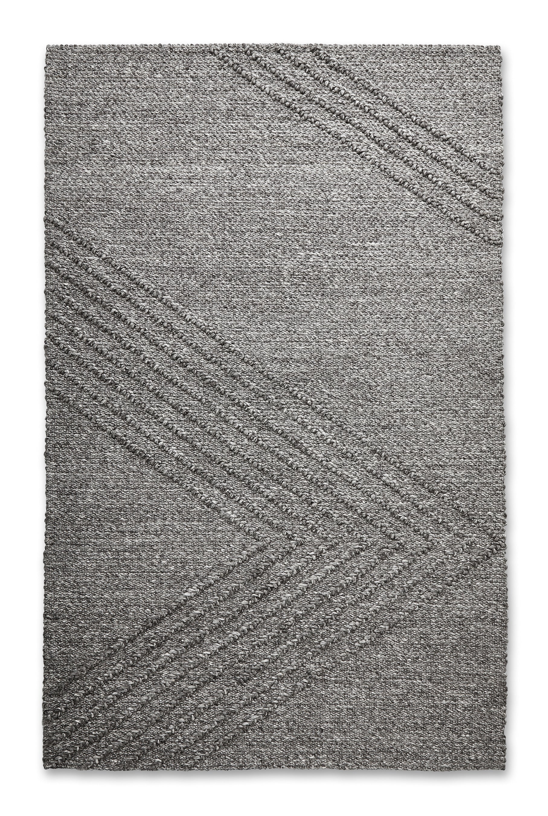 The Avro Rug by Gus Modern is a rectangular gray minimalist rug featuring a subtle chevron pattern with raised diagonal lines, offering a simple, modern look ideal for contemporary spaces.