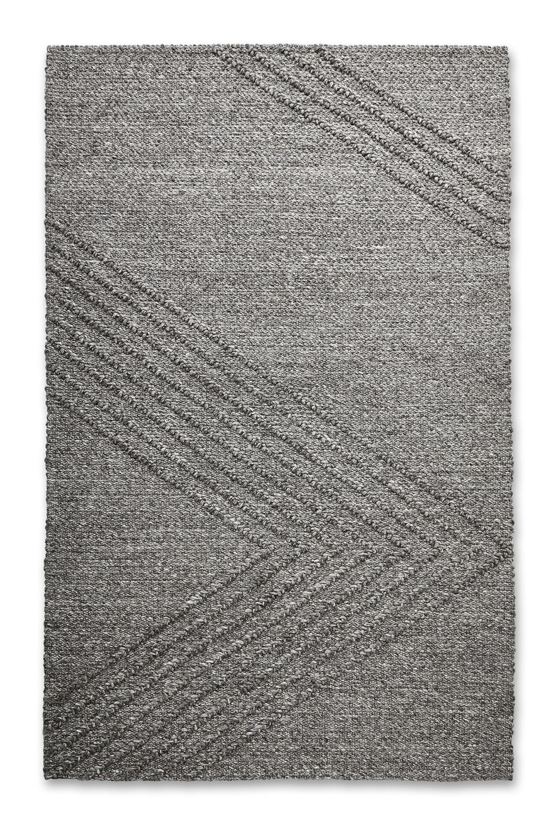 The Avro Rug by Gus Modern is a rectangular gray minimalist rug featuring a subtle chevron pattern with raised diagonal lines, offering a simple, modern look ideal for contemporary spaces.