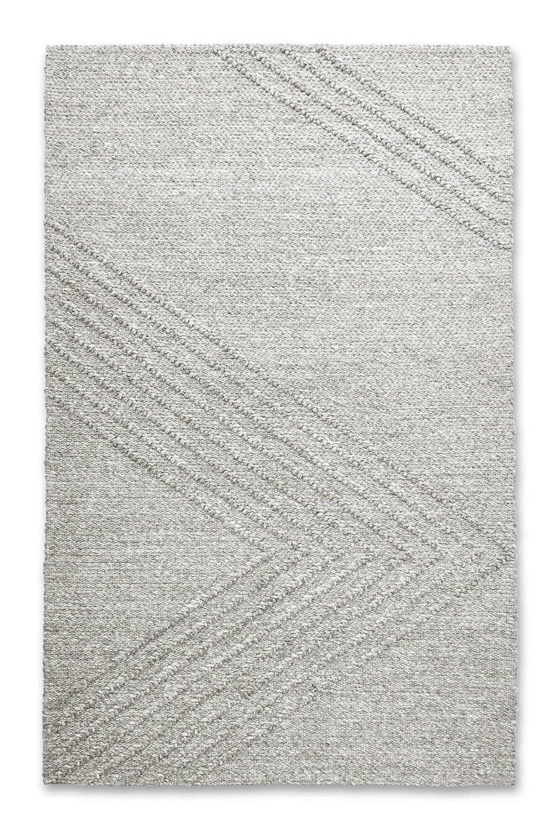 The Avro Rug by Gus Modern is a light gray, minimalist hand-knotted New Zealand wool rug featuring subtle diagonal lines that form large chevron shapes, lending a modern and sophisticated touch to any space.