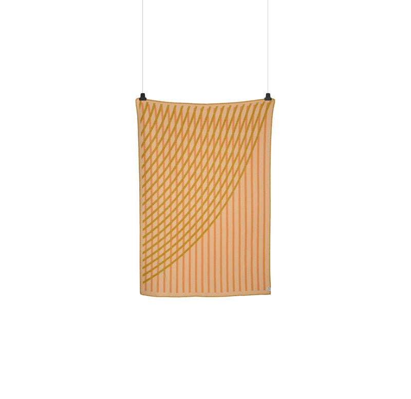 The BISLETT Throw by Roros, featuring a beige and orange geometric pattern reminiscent of the moiré phenomenon, hangs elegantly against a white background, secured by two clips.