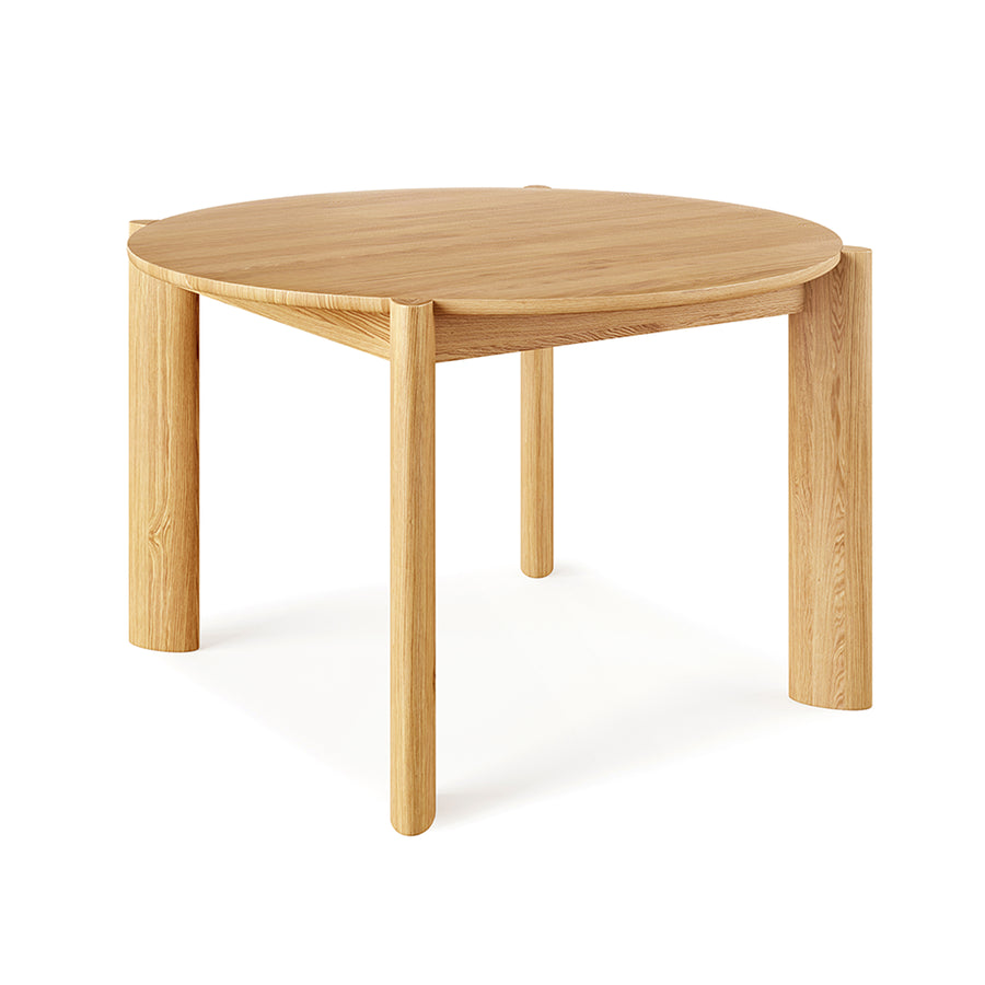 The Bancroft Dining Table Round by Gus Modern is a solid wood dining table with four thick cylindrical legs and a natural light wood finish, shown with its minimalist design against a white background.