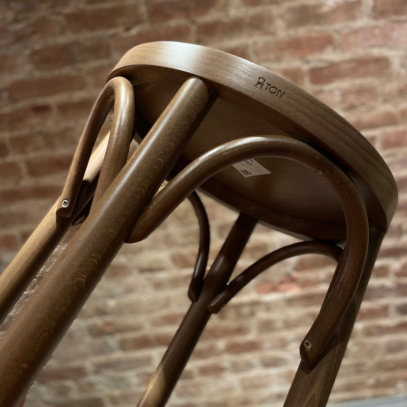 The Barstool 73 by TON, visible from a low angle against a brick wall, boasts beech leg joints and curved legs. It features an upholstered seat with a smooth, polished finish and sturdy appearance.