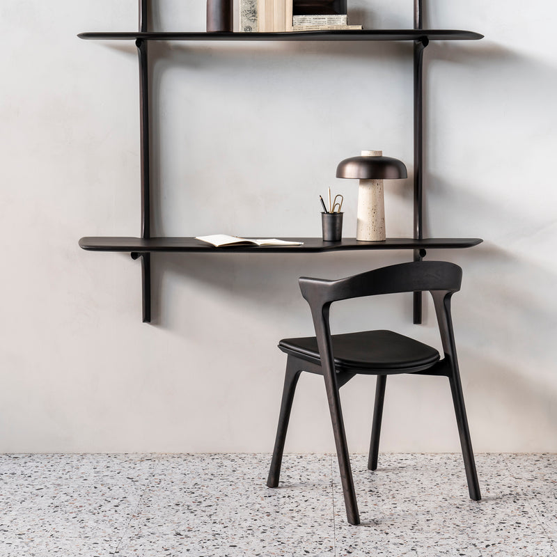 Bok Dining Chair - Upholstered in black varnished oak with black leather seat, placed in minimalist room with floating desk and lamp.