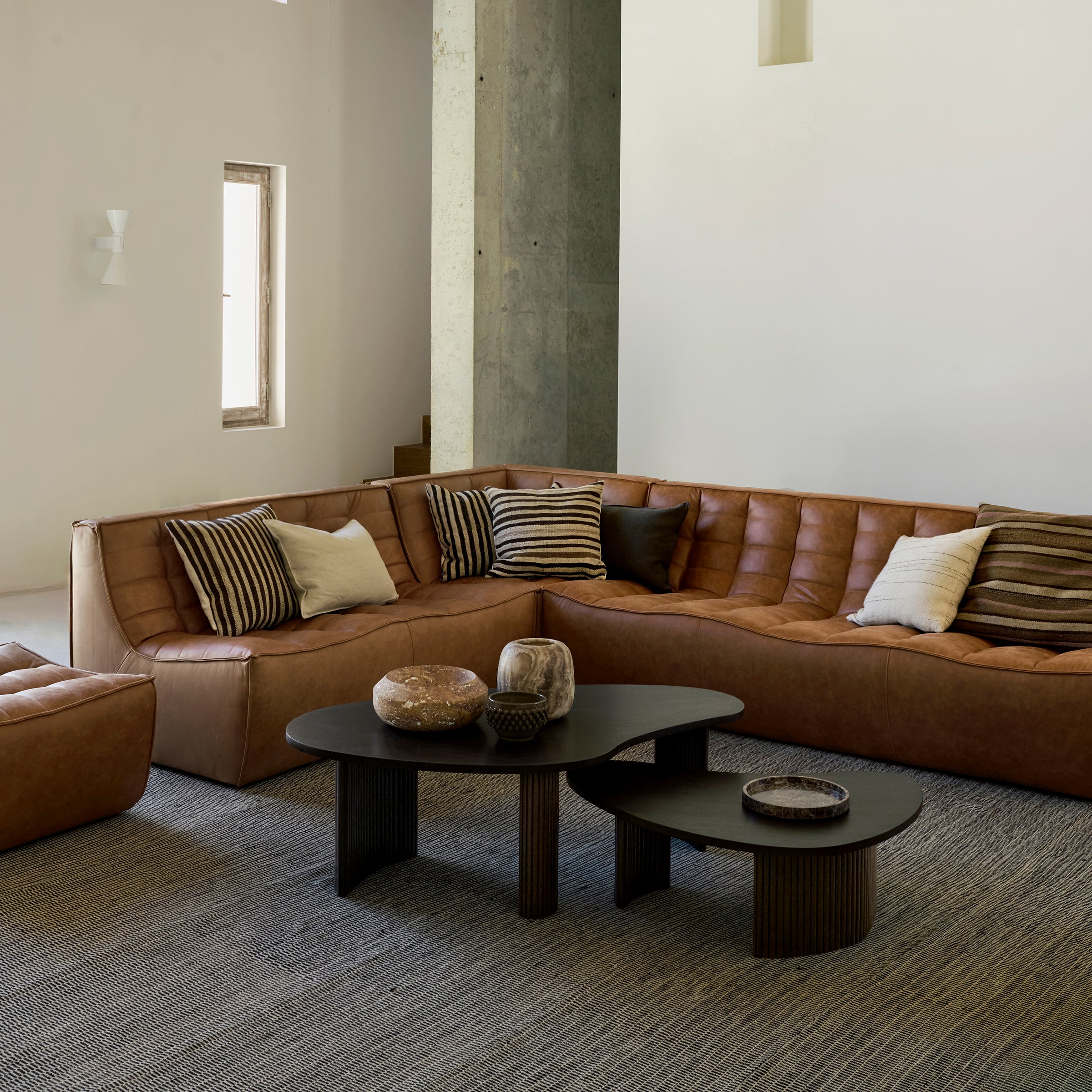 Boomerang Coffee Table in dark wood with smooth curves in a modern living room setting with brown leather sofas.