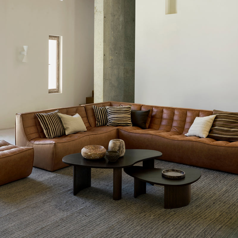 Boomerang Coffee Table in dark wood with smooth curves in a modern living room setting with brown leather sofas.