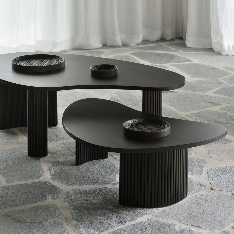 Boomerang Coffee Table set with sleek black curved tops and ribbed cylindrical bases on stone floor near sheer curtains